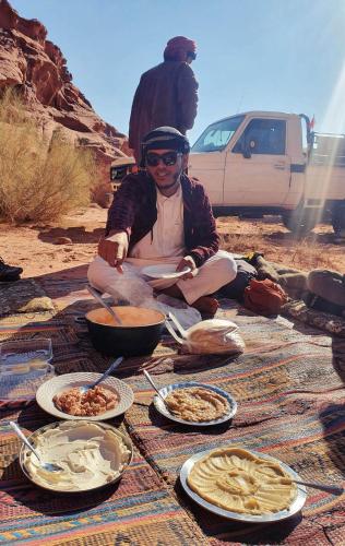 a man sitting on a blanket with plates of food at Wadi Rum Travel camp in Wadi Rum