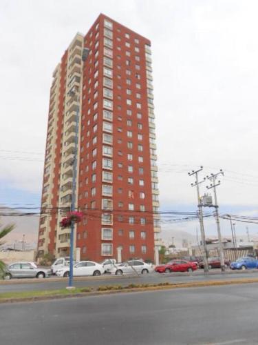 a tall red building with cars parked in a parking lot at Amoblados MyK Portal Heroes in Iquique