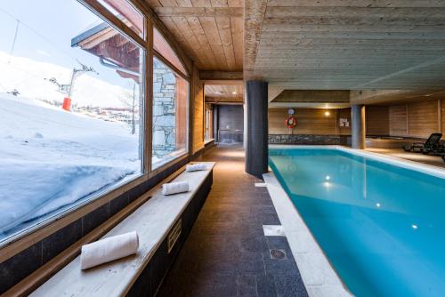 a swimming pool in a building with a large window at Lagrange Vacances Les Hauts de Comborcière in La Toussuire