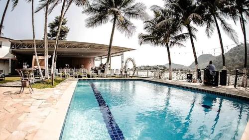 une piscine avec des palmiers et un homme assis à côté dans l'établissement Le Partie, à Angra dos Reis