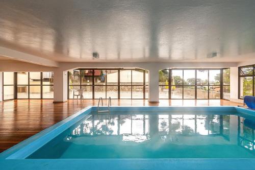 a large swimming pool in a building with a large window at Rosa Edifício Mirante da Colina in Gramado