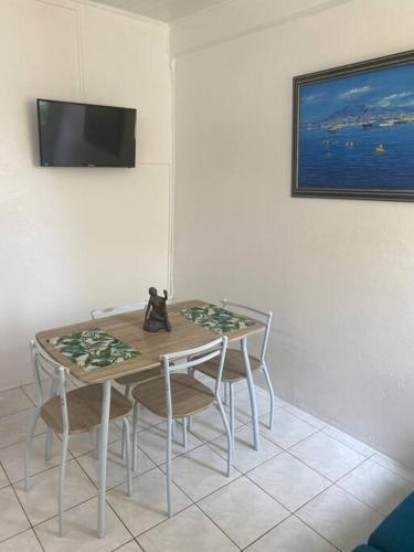 a dining room table with chairs and a television on a wall at Appartement Osiris 2 in Fort-de-France