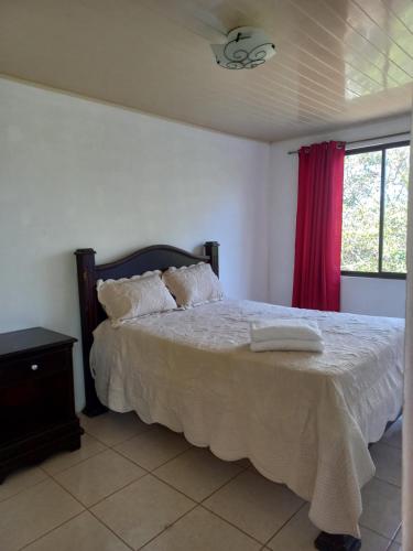 a bedroom with a bed with white sheets and a window at Casa Montañas Nicoyanas in Juan Díaz