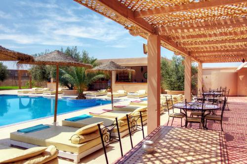 eine Terrasse mit Tischen und Stühlen sowie einem Pool in der Unterkunft La Maison Des Oliviers in Marrakesch