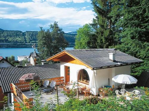 a small house with a patio with chairs and an umbrella at Ferienwohnung Schellander Privatstrand in Velden am Wörthersee