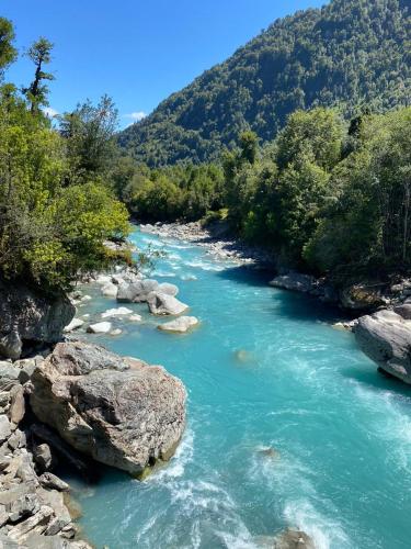 a river with blue water and rocks and trees at Cabañas & Habitaciones Del Alto in Hornopiren