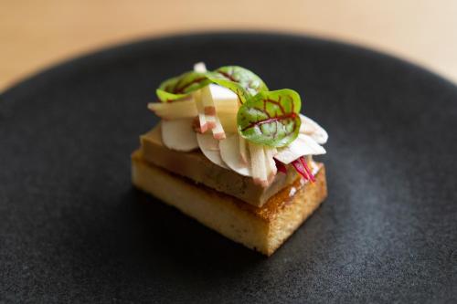 a piece of food sitting on a black plate at Yoichi LOOP in Kurokawamachi