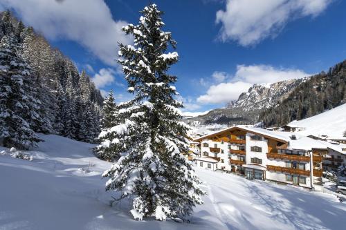 a snow covered tree in front of a lodge at Savoy Dolomites Luxury & Spa Hotel in Selva di Val Gardena