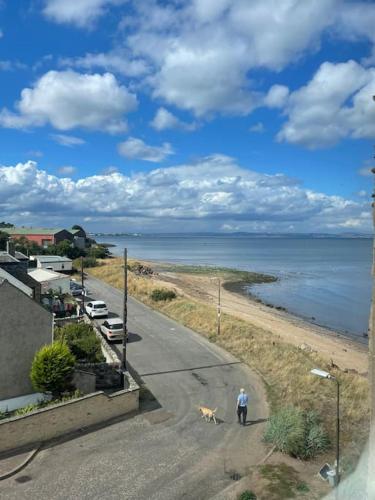 a man walking a dog down a road next to the ocean at Beachfront Treasure in Musselburgh