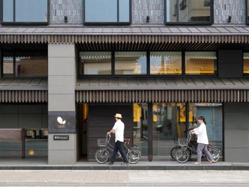 twee mensen lopen met hun fiets voor een winkel bij Dhawa Yura Kyoto - Banyan Group in Kyoto