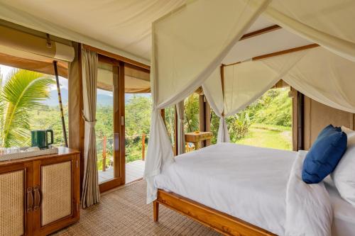 a bedroom with a canopy bed and a balcony at Nadi Nature Resort - Adults Only in Tabanan
