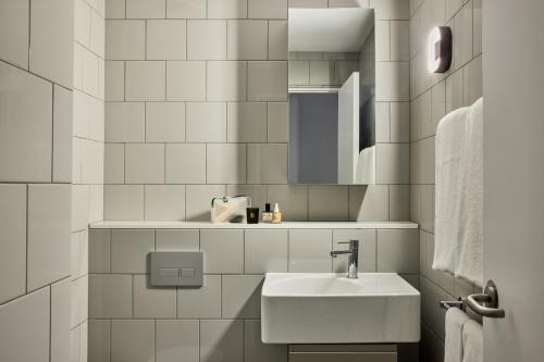a white tiled bathroom with a sink and a mirror at Punthill Parramatta in Sydney
