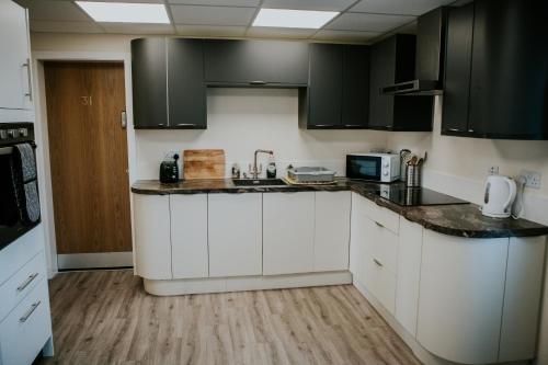a kitchen with white cabinets and black appliances at Uist Travel Accommodation in Daliburgh