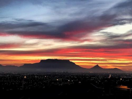 a sunset over a city with a mountain in the background at Cozy spacious loft on 4th Avenue in Cape Town