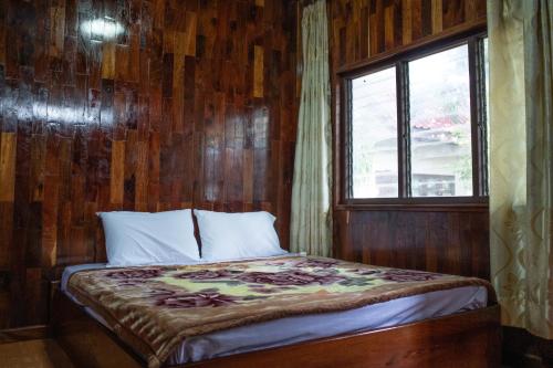 a bed in a wooden room with a window at Song Lao Guesthouse in Thakhek