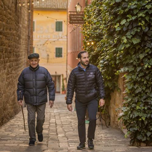 two men walking down a street in an alley at PALAZZO DEL CAPITANO Wellness & Relais - Luxury Borgo Capitano Collection in San Quirico dʼOrcia