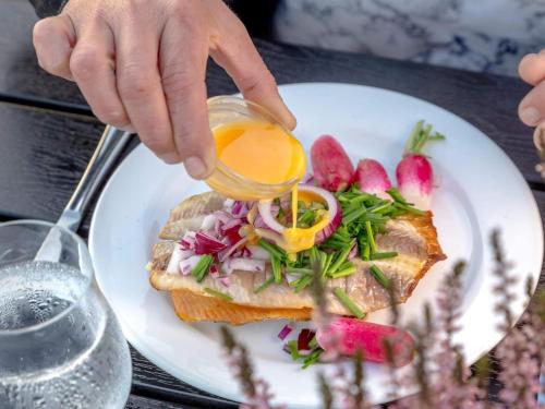 a person sprinkling sauce on a sandwich on a plate at 5 person holiday home on a holiday park in Gudhjem in Gudhjem