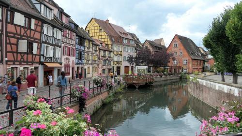 a river in a town with buildings and flowers at Un balcon sur les toits in Beblenheim