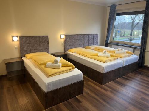 2 bedden in een slaapkamer met gele lakens en een raam bij M&M Hotel - Seevetal in Seevetal