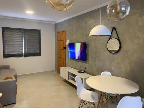 a dining room with a table and a tv on a wall at Apto 1o andar novo 2 Dorm - próximo ao centro in Poços de Caldas