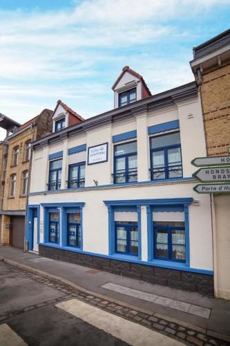 a white building with blue windows on a street at Gite Bergues Centre in Bergues