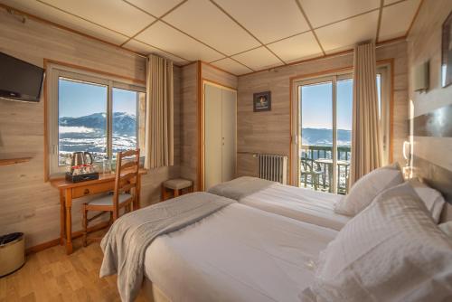 a bedroom with a bed and a desk and windows at Hotel des Pyrénées in Font-Romeu
