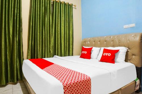 1 dormitorio con cama con almohadas rojas y cortinas verdes en SUPER OYO 92075 Sky Residence Mawar en Sunggal