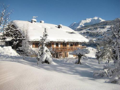 une maison recouverte de neige avec des arbres devant elle dans l'établissement Ferme Vauvray, à Megève
