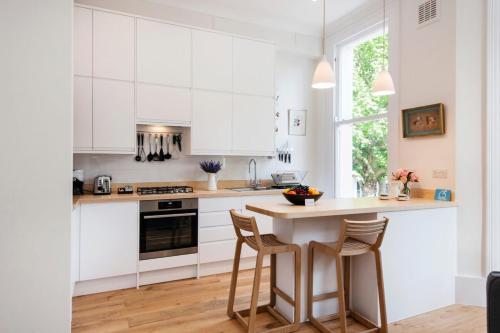 ロンドンにあるThe Stunning Philbeach Garden Apartmentの白いキャビネットとテーブル(スツール付)が備わるキッチン