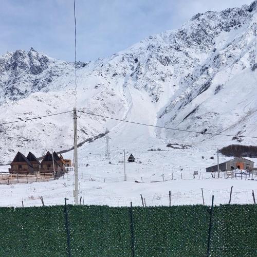 a snow covered mountain with houses and a fence at mood villa Kazbegi in Stepantsminda