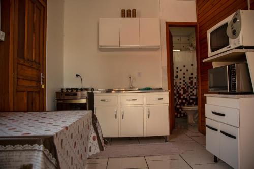 cocina con armarios blancos, fregadero y microondas en Chale Namaste 3, en Palhoça