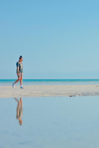 a man walking on the beach with his reflection in the water at Hotel Encanto Holbox Beach Front in Holbox Island