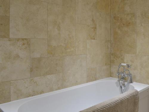 a bath tub in a bathroom with a tile wall at The Granary in Tiverton