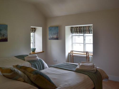 two beds in a room with two windows at Clematis Cottage in Burnsall