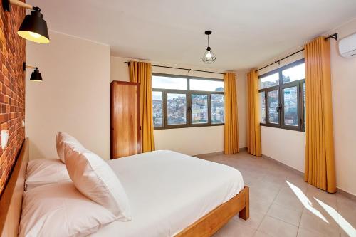 a bedroom with a bed and two windows at La Pergola - Appartement Hôtel in Antananarivo