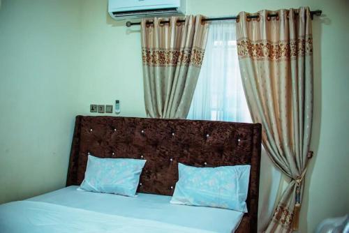 a bed with a headboard and a window with curtains at Superb 2-Bedroom Duplex FAST WiFi+24Hrs Power in Lagos