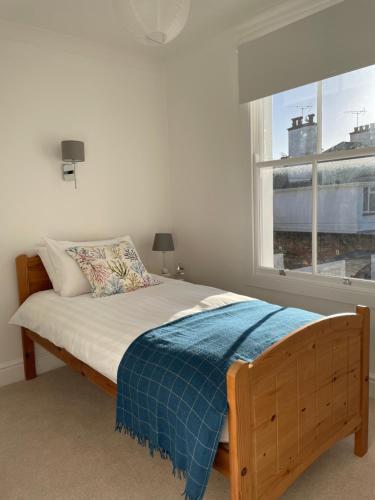 1 dormitorio con 1 cama con manta azul y ventana en Wren House, en Sidmouth