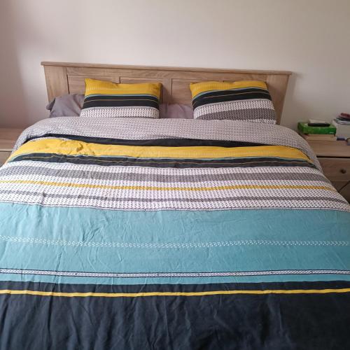 een bed met een blauwe en gele deken en 2 kussens bij Maison pour location de chambre 24H et GP in Aigné