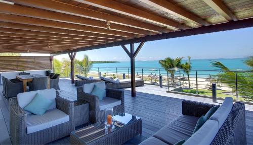 una terraza al aire libre con sillas, mesas y el océano en Paradise Beach by Horizon Holidays en Pointe d'Esny