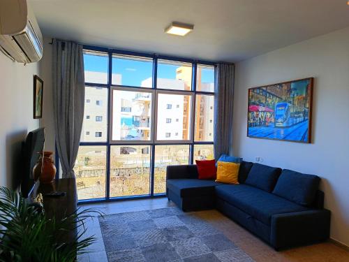 a living room with a blue couch and a large window at By the Sea in Ashkelon