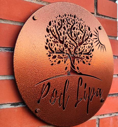 a metal sign with a tree on a brick wall at Agroturystyka Pod Lipa in Boreczno