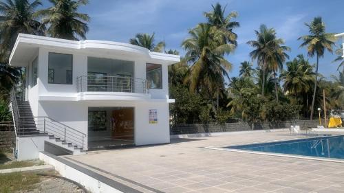 a white house with a swimming pool and palm trees at Hotel Agni in Krishnagiri