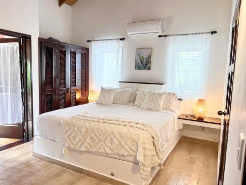 um quarto com uma cama branca com lençóis brancos e janelas em Playa Bonita 4 minute walk from our private Villa Anantara Bonita em Las Terrenas