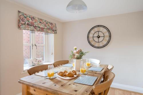 a dining room with a wooden table with a clock on the wall at Rose Cottage, Snettisham, Norfolk in Snettisham