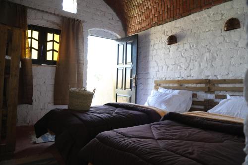 a bedroom with two beds and a brick wall at Krouma Camp & Ecolodge in Naj‘ al Maḩaţţah