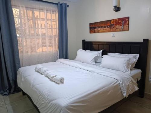 a large bed with white sheets and a window at Stylish 2 bedroom apartment in Nairobi