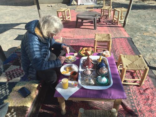 una mujer sentada en una mesa con una bandeja de comida en Nomad Bivouac en Merzouga