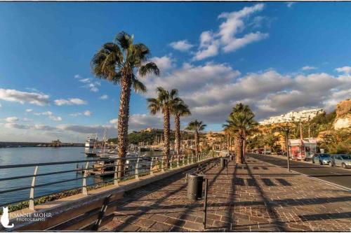 a boardwalk with palm trees and a body of water at New, Modern Ground Floor Apartment with Pool in Għajnsielem