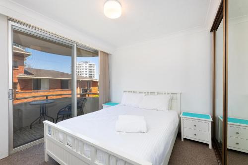 a bedroom with a white bed and a balcony at Sandbar 103 in Forster