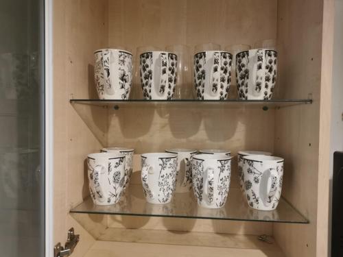 eine Gruppe weißer Tassen auf Regalen in einer Küche in der Unterkunft Ella's Place in Luton